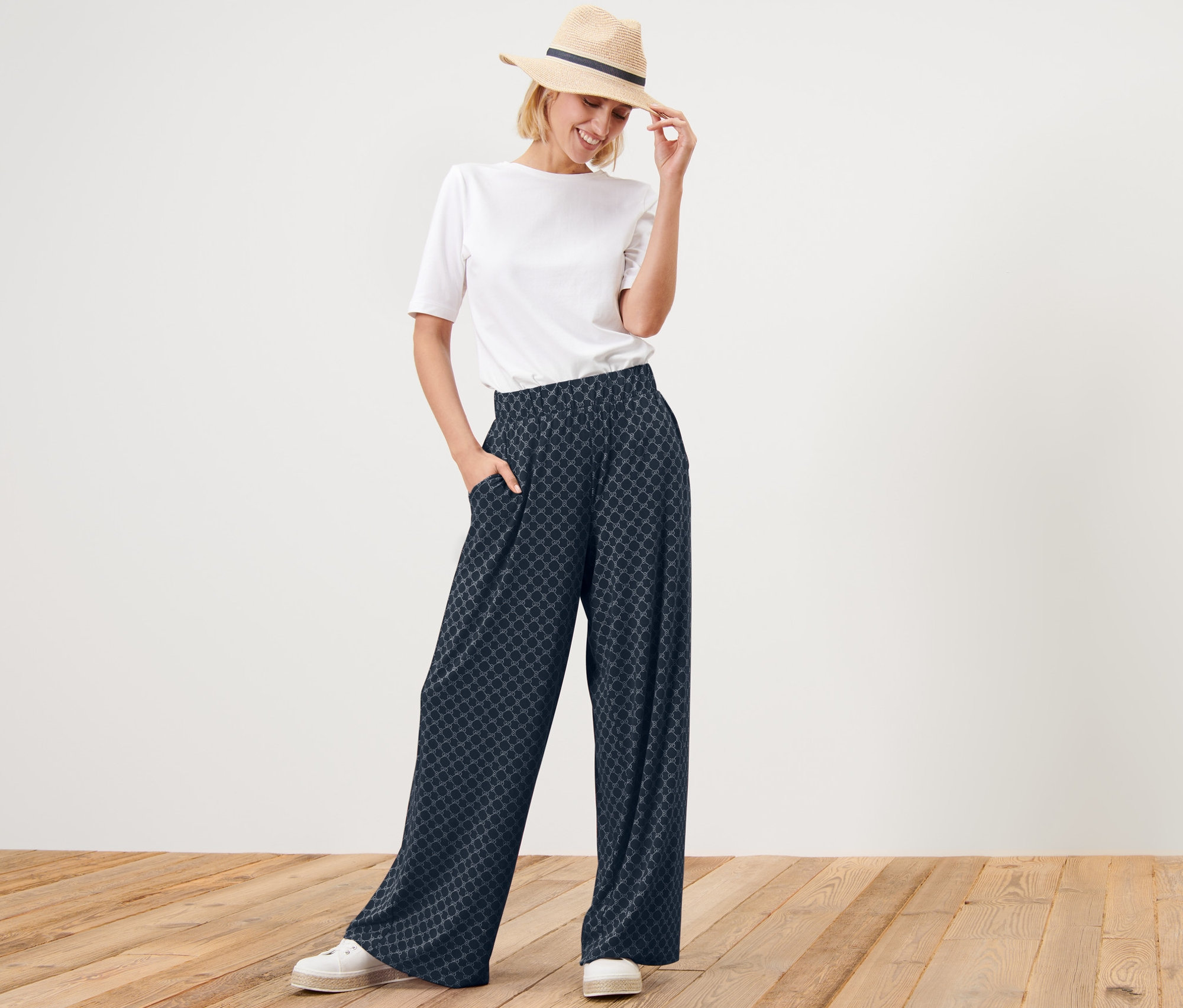 Femme posant en pantalon palazzo imprimé bleu foncé et t-shirt blanc.