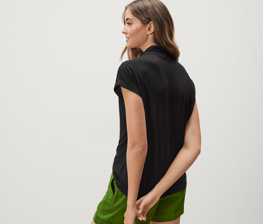 Vue arrière d'une femme portant une blouse noire à encolure en V et un short vert.