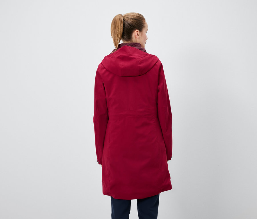 Vue de dos d'une femme avec une queue de cheval portant une veste à capuche rouge et un pantalon bleu marine.