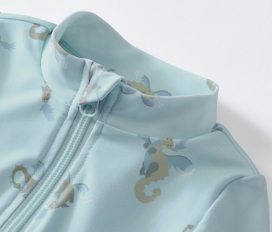 Gros plan sur une combinaison bleue pour bébé avec protection UV 80, motif dragon et fermeture éclair.