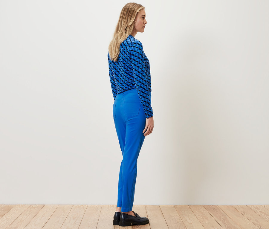 Une femme se tient de côté et porte un pantalon en bengaline bleu cobalt.