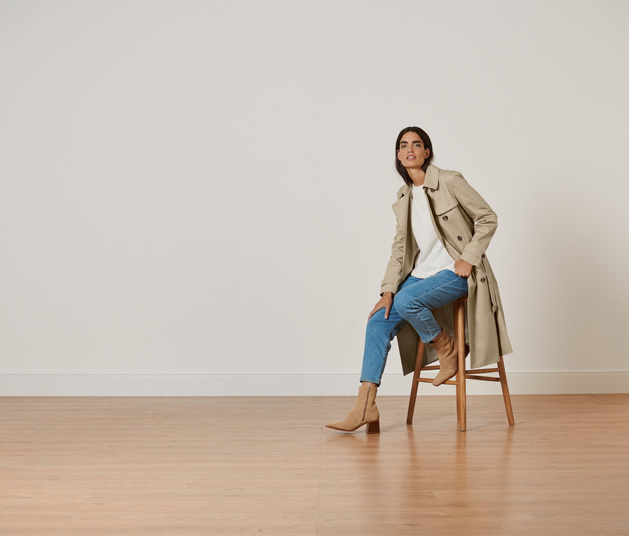 Femme assise sur un tabouret portant un trench-coat.