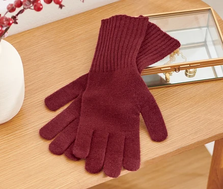 Des gants en maille avec de la laine sont posés sur une table en bois à côté d'un vase avec des baies rouges et une boîte à bijoux.