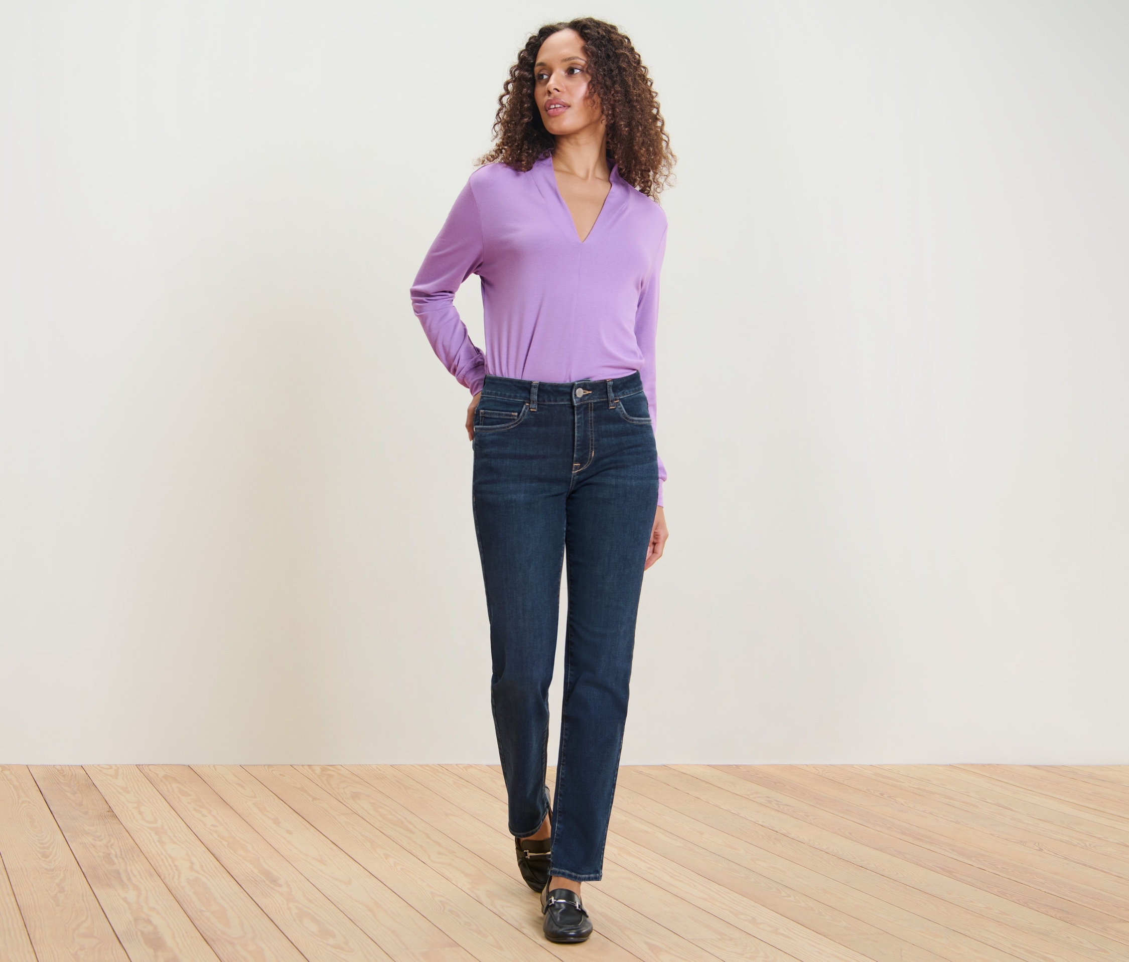Une femme pose, portant un jean droit bleu foncé – Fit « Kira » et un haut violet.