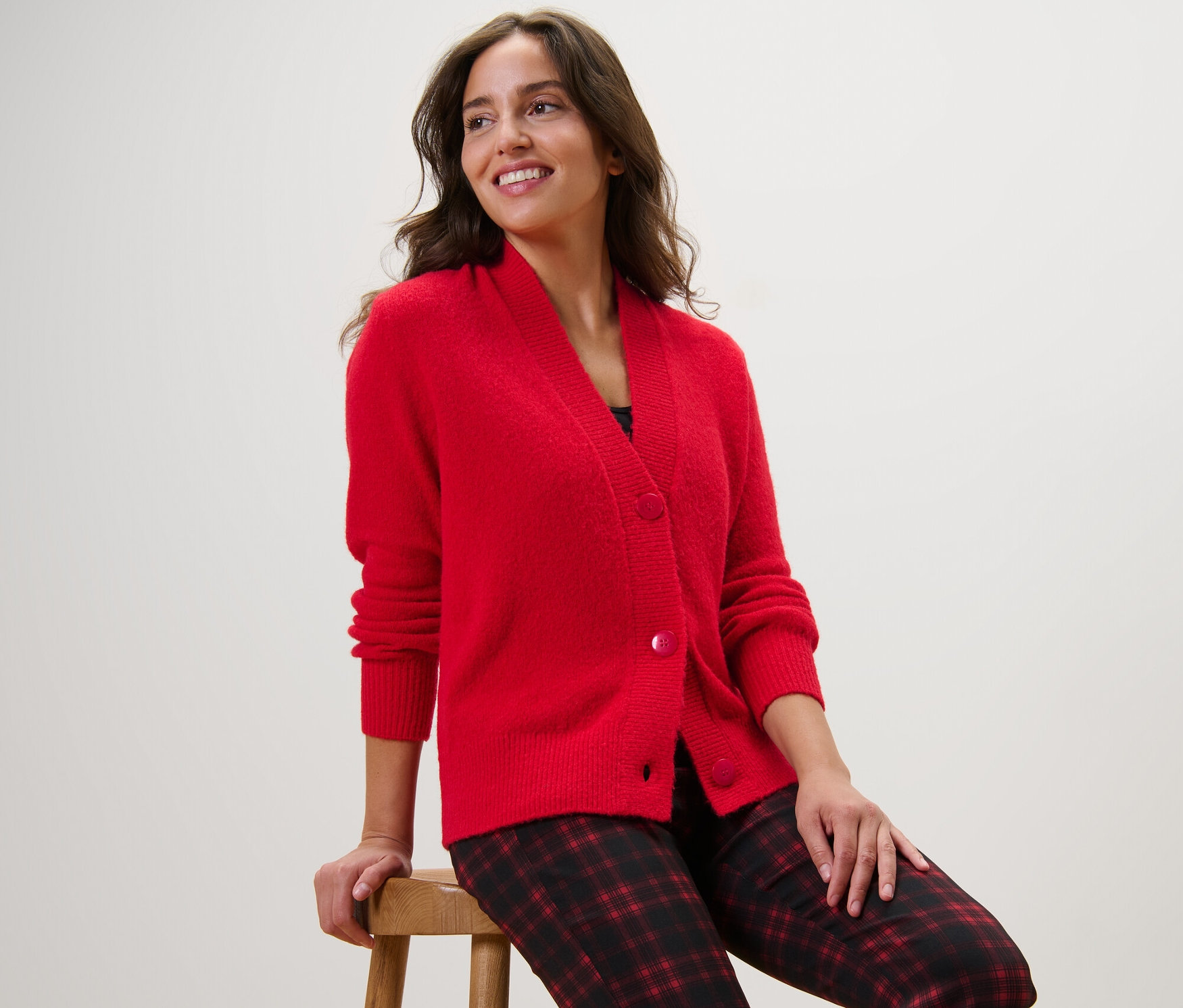 Femme assise sur un tabouret portant un cardigan rouge.