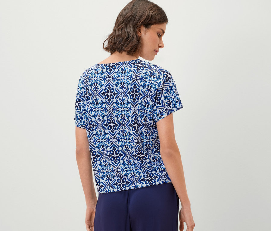 Une femme porte un chemisier bleu imprimé et un pantalon ample.