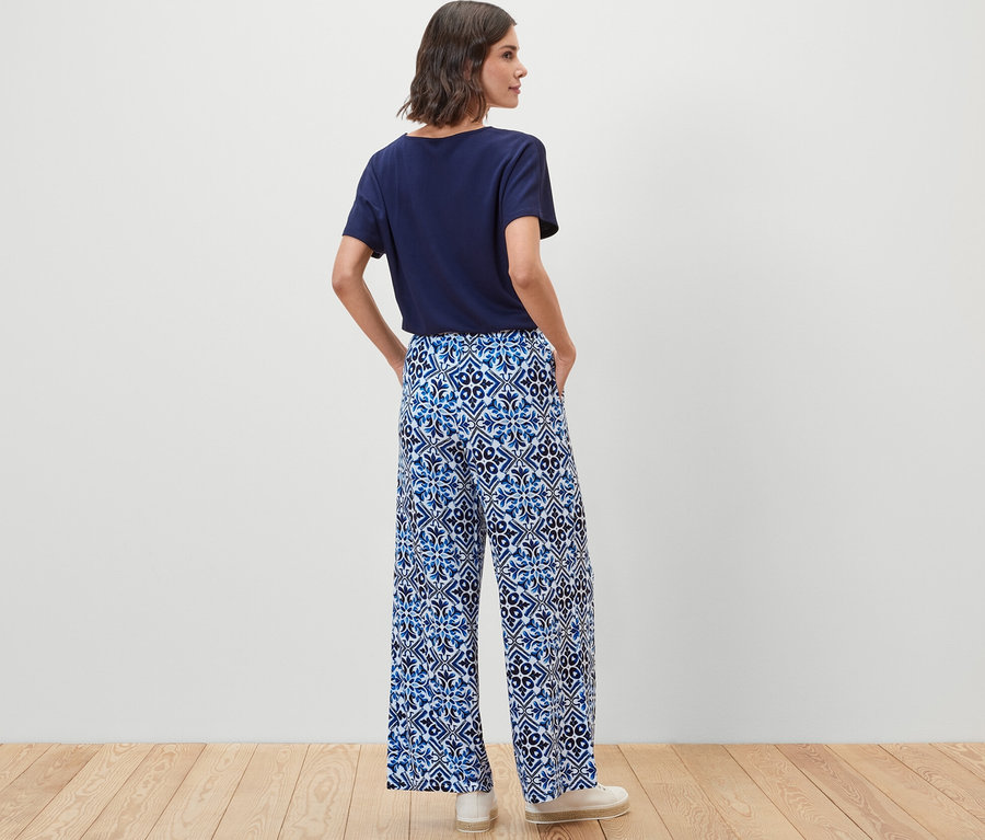 Une femme, vue de dos, porte un pantalon palazzo imprimé bleu.