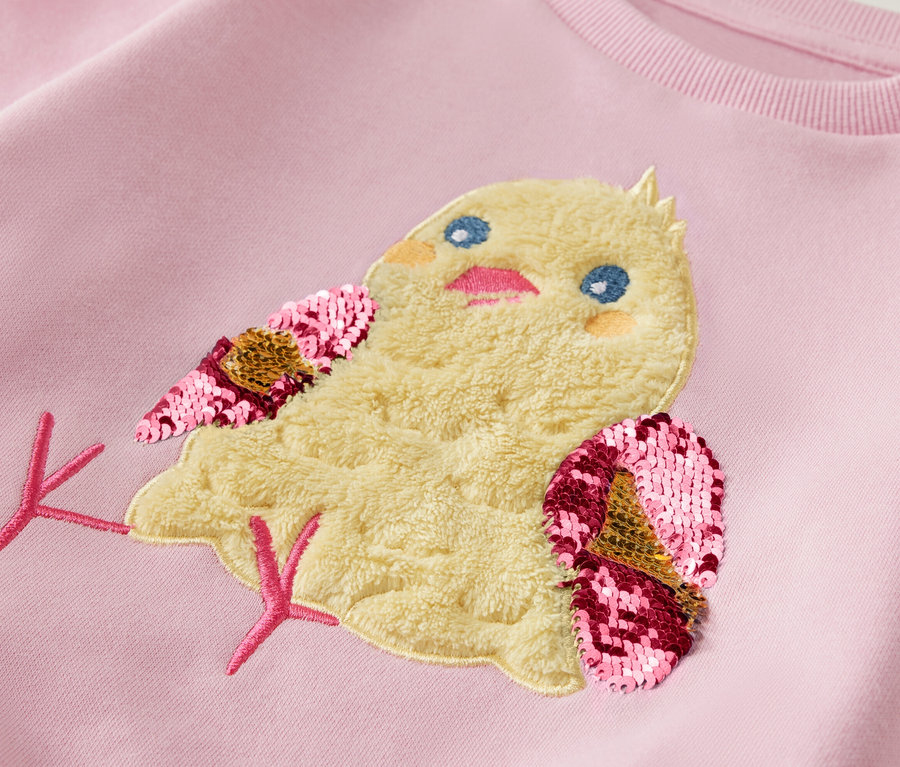 Sweat-shirt rose clair avec un patch poussin avec des ailes à paillettes.
