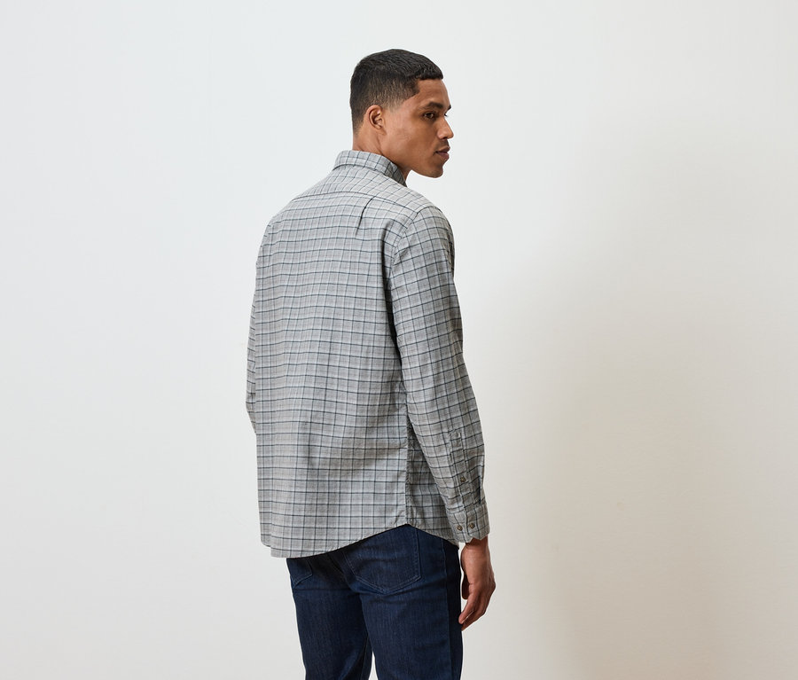 Un homme en chemise à carreaux et jeans sombres, dos au spectateur.