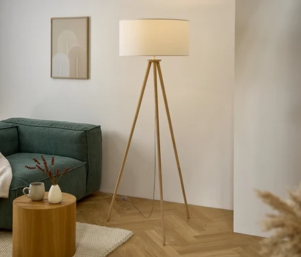 Salon avec canapé, table en bois, lampadaire trépied et œuvre d'art au mur.