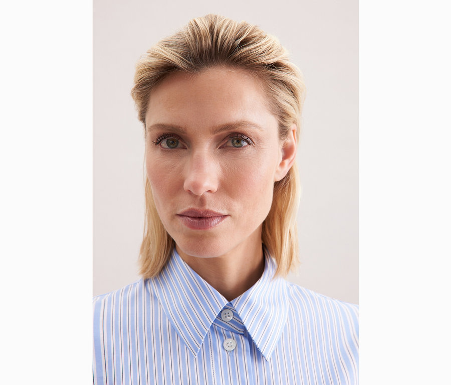 Gros plan d'une femme blonde portant une chemise oversize rayée bleu et blanc Seidensticker.