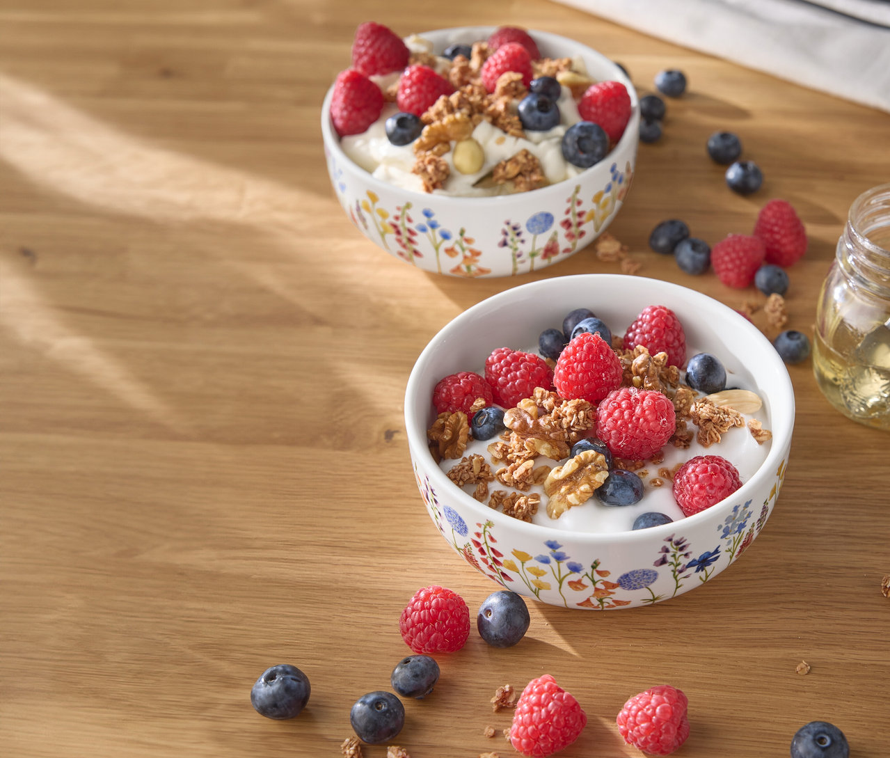 Deux bols de yaourt avec des framboises, des myrtilles et des noix sur une table en bois.