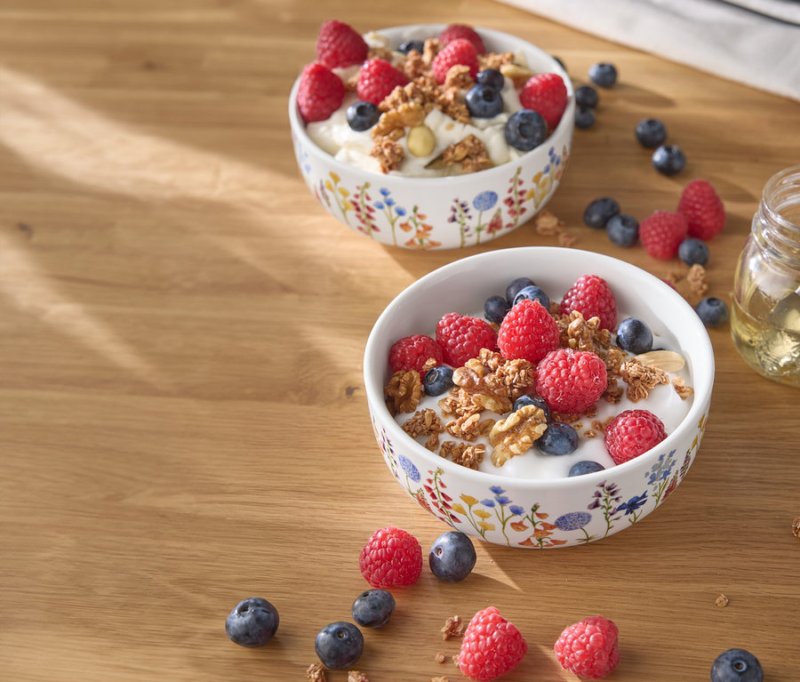 Deux bols de yaourt avec des framboises, des myrtilles et des noix sur une table en bois.