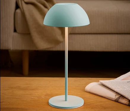 Une lampe turquoise est posée sur une table à côté d'un journal.