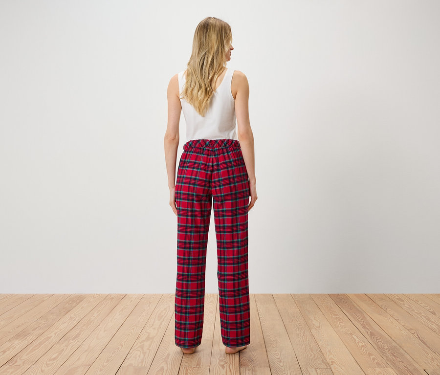 Une femme, vue de dos, porte un débardeur blanc et un pantalon à carreaux rouge.