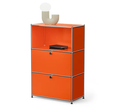 Un système d'étagères modulaires orange avec deux tiroirs et une étagère ouverte sur laquelle reposent deux livres noirs et une lampe beige.