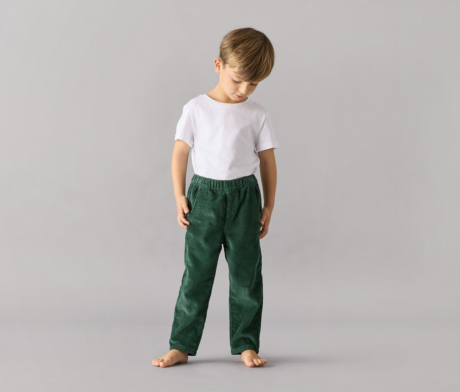Un garçon debout porte un pantalon à enfiler vert pour enfants – Coupe « Mika » et un t-shirt blanc.