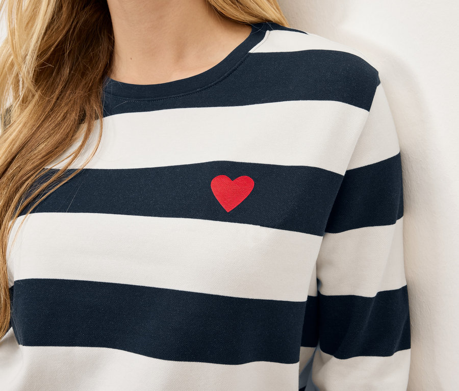 Gros plan sur le torse d'une femme portant un t-shirt rayé à manches longues avec un petit cœur rouge sur la poitrine.