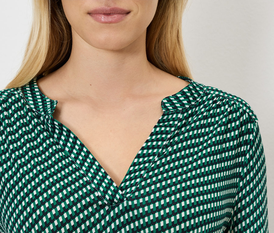 Gros plan d'une femme blonde portant un chemisier à carreaux vert et blanc.