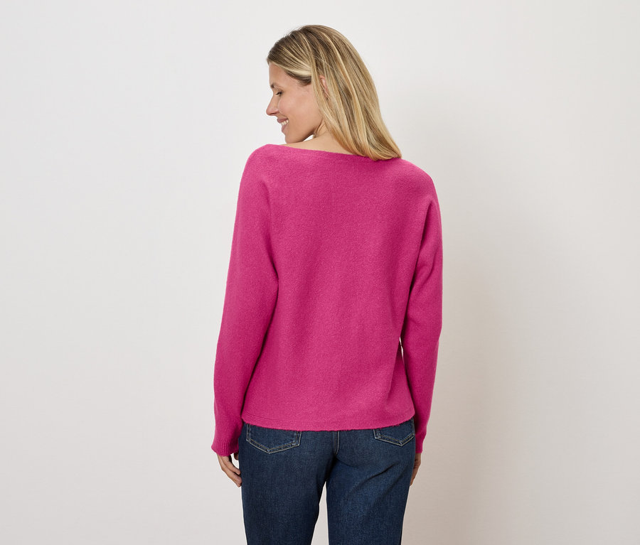 Une femme regarde vers la gauche, portant un pull rose et un jean.