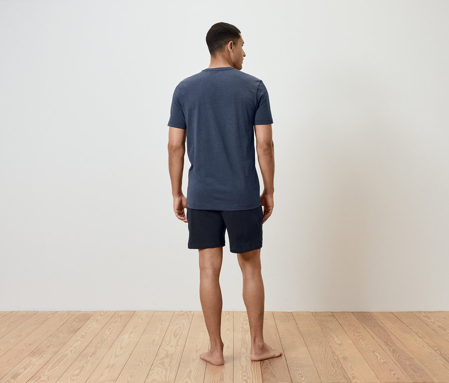 Un homme debout, dos à la caméra, portant un t-shirt bleu et un short noir.