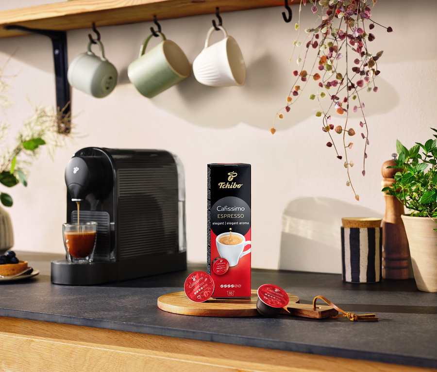 Une machine à expresso verse du café dans un verre à côté d'un paquet de Cafissimo Espresso elegant – 10 capsules.