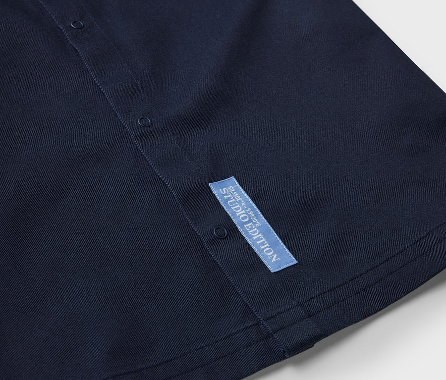 Gros plan sur une chemise pour enfant bleu marine avec des boutons et une étiquette Studio Edition.