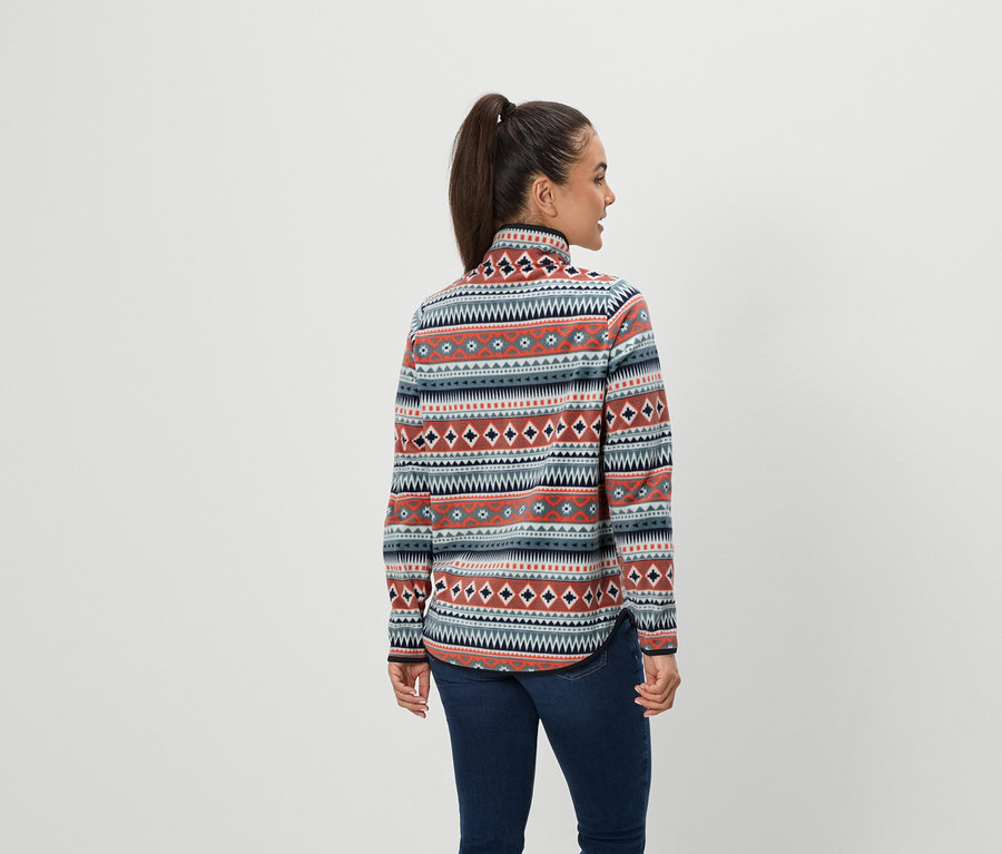 Une femme aux cheveux bruns attachés en queue de cheval se tient dos à l'appareil photo, portant un jean bleu et un pull en polaire à motifs.