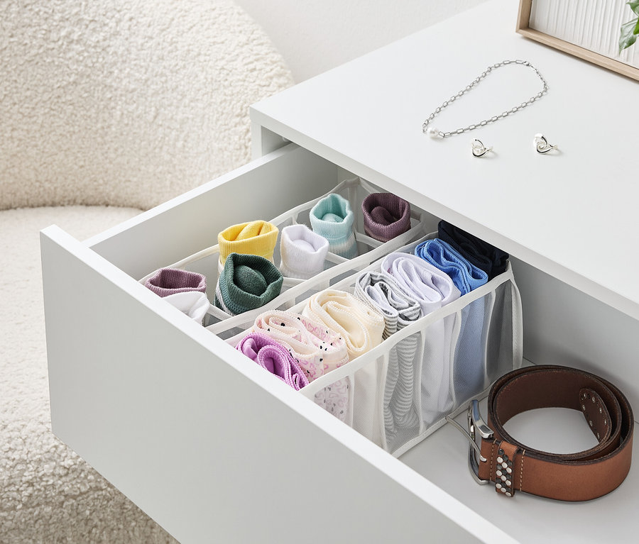 Un tiroir ouvert d'une table blanche avec un organisateur rempli de chaussettes et de sous-vêtements colorés, à côté duquel se trouve une ceinture marron.