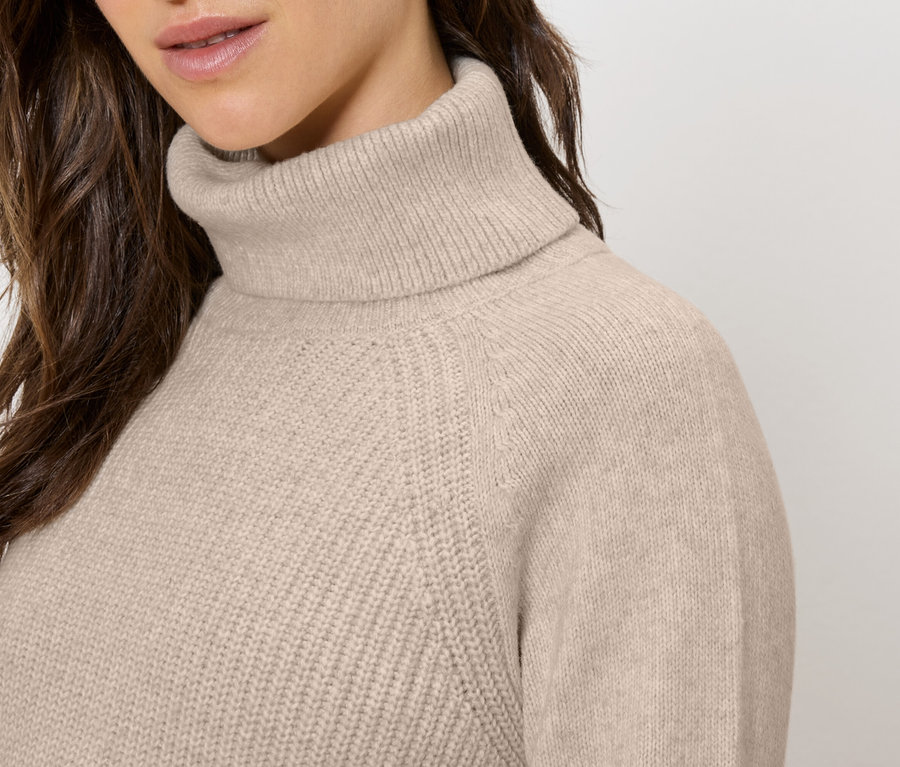 Gros plan d'une femme portant un pull à col roulé beige.
