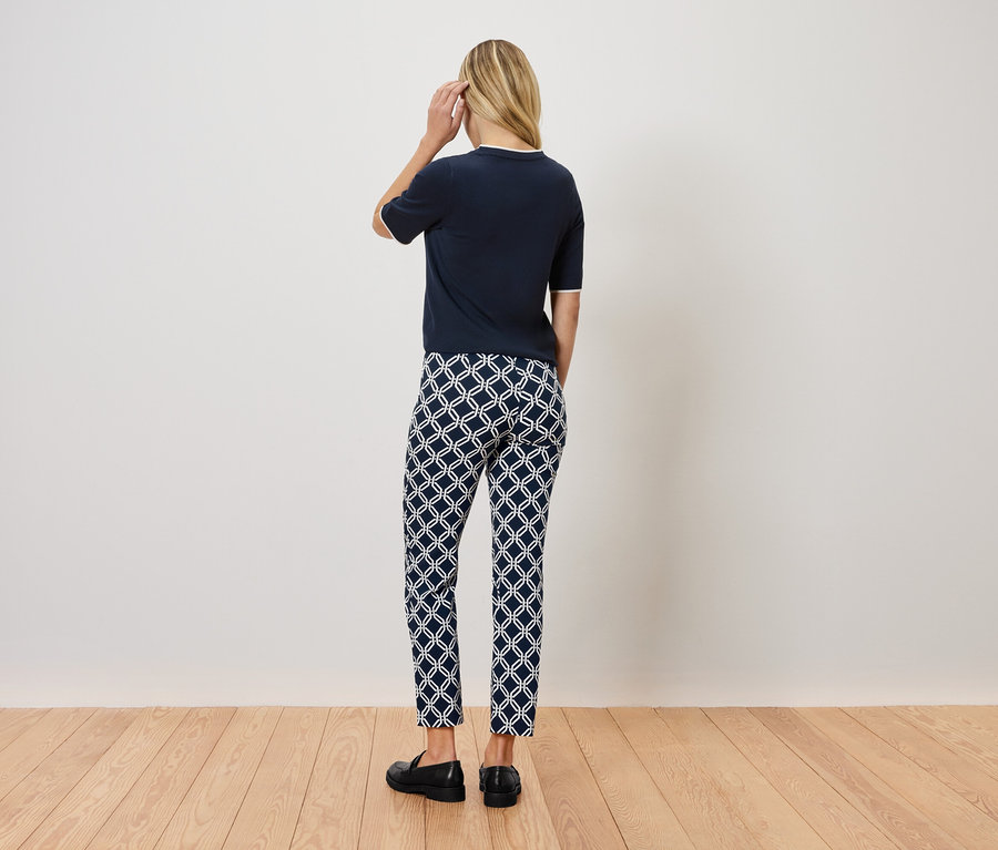 Une femme, vue de dos, porte un haut bleu marine, un pantalon à motifs et des chaussures noires.