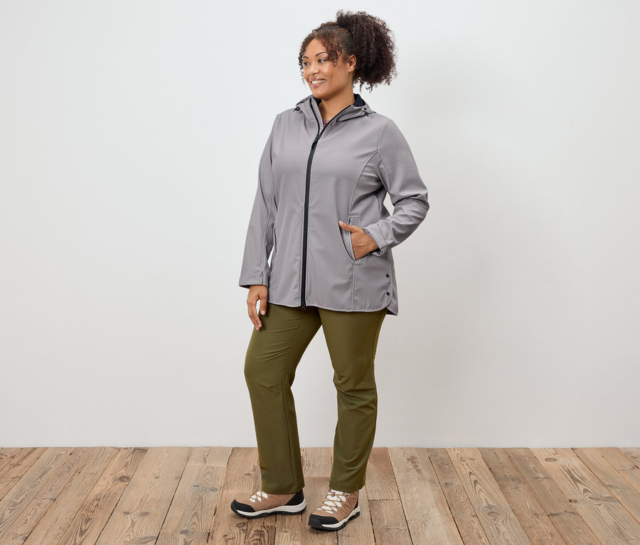 Femme posant en veste grise, pantalon vert et chaussures de sport.