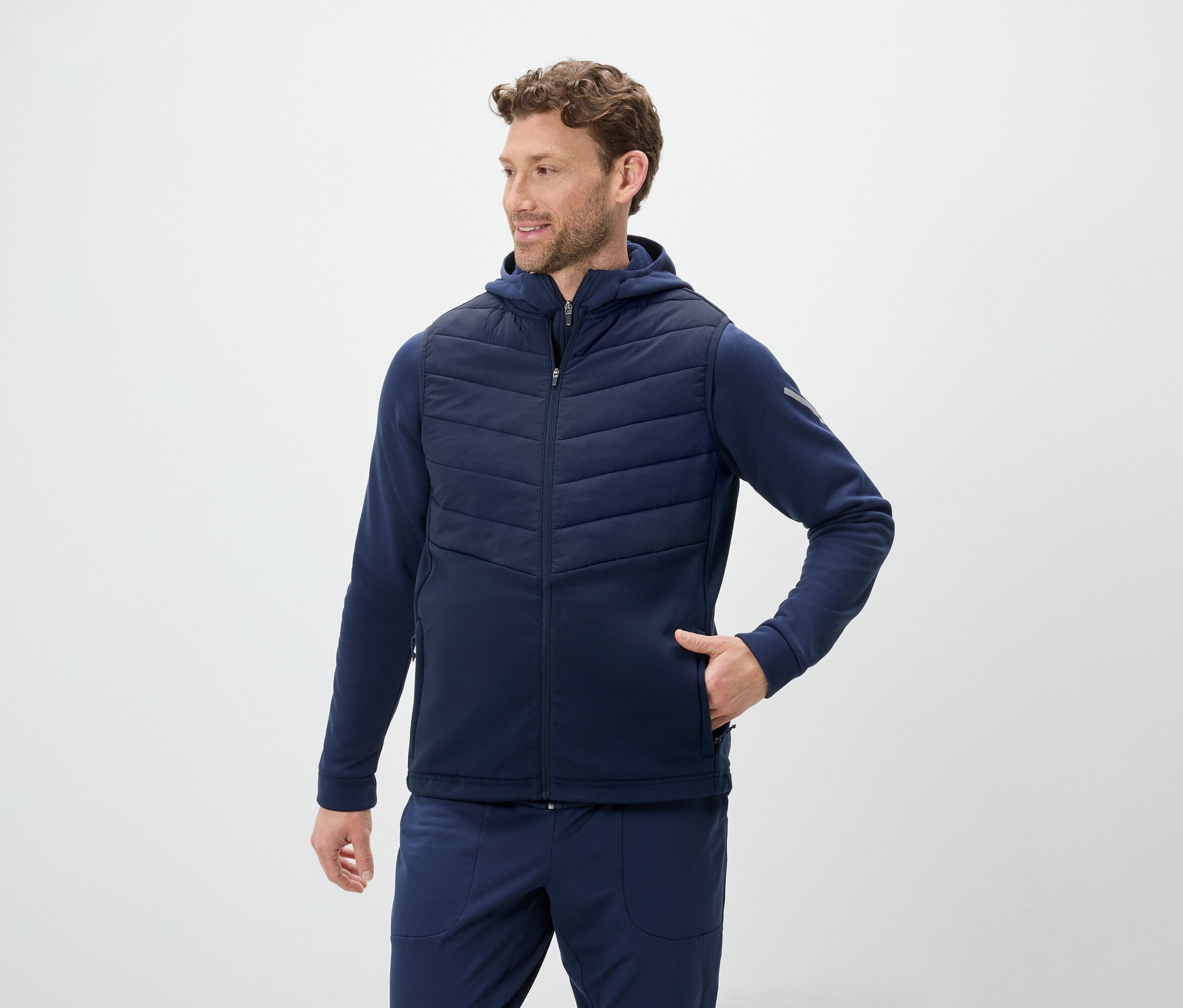 Un homme porte un gilet bleu à capuche et un jogging bleu.