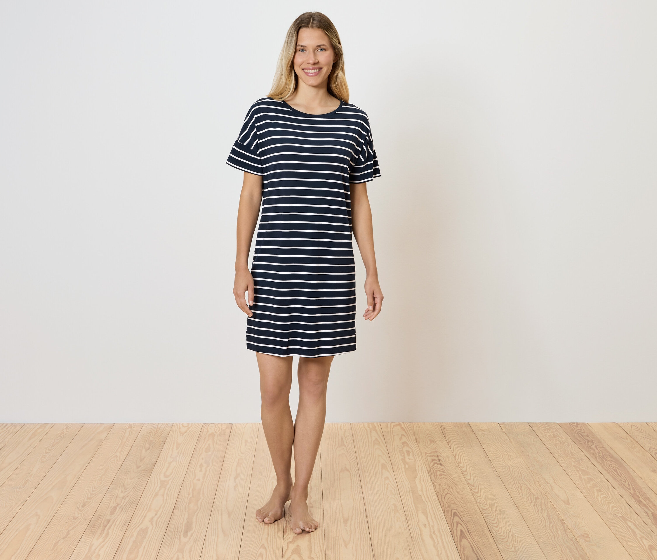 Une femme se tient sur un plancher en bois et porte une robe t-shirt rayée.