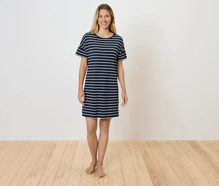 Une femme se tient sur un plancher en bois et porte une robe t-shirt rayée.
