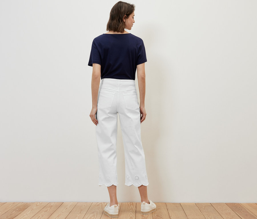 Une femme, vue de dos, porte un t-shirt bleu marine et un jean blanc avec broderie ajourée.