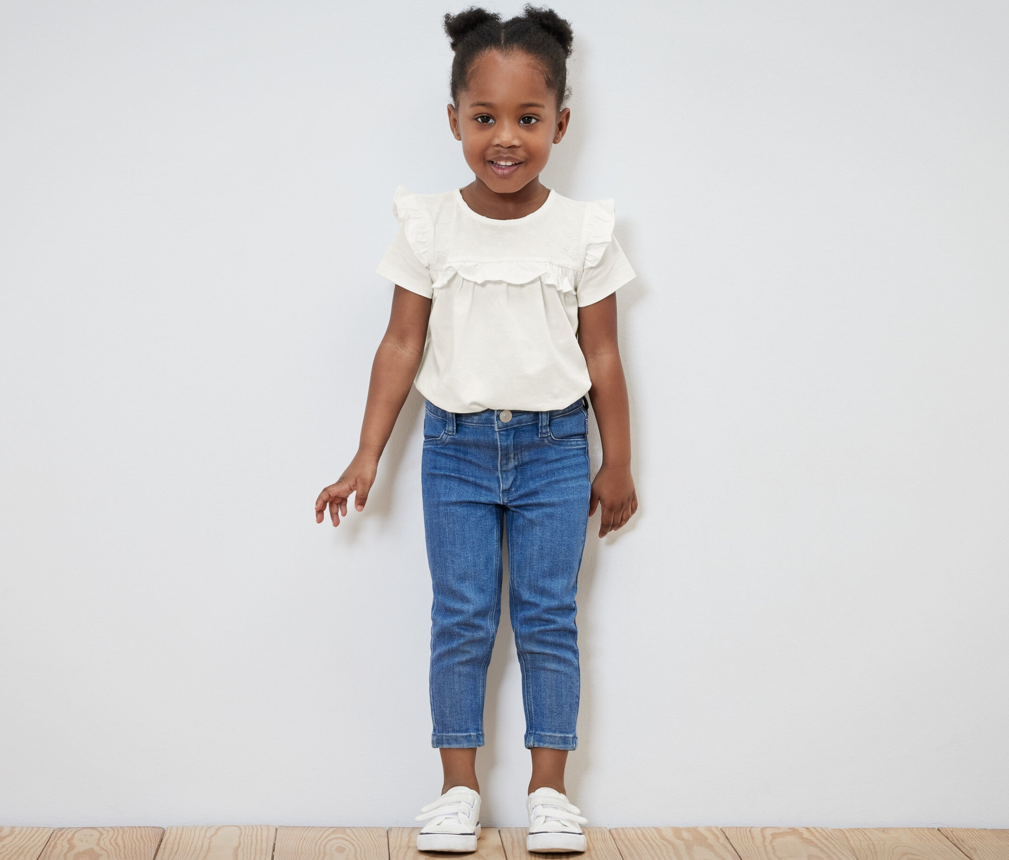 Petite fille souriante posant dans un t-shirt clair pour enfants et un jean bleu.