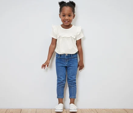 Petite fille souriante posant dans un t-shirt clair pour enfants et un jean bleu.
