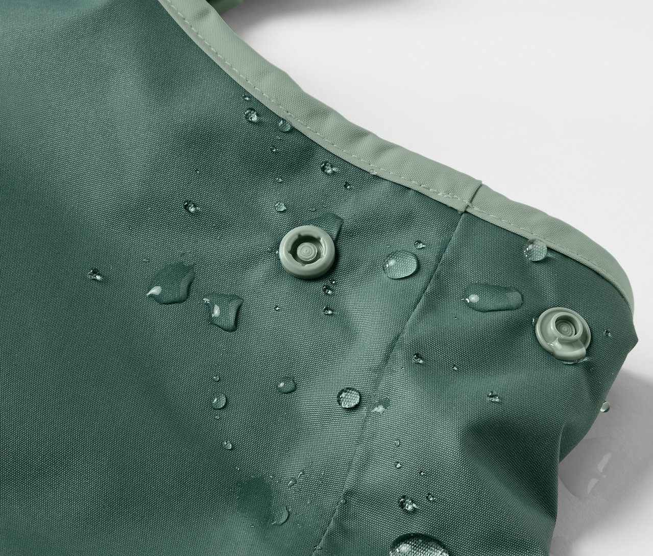 Gros plan sur un pantalon de pluie thermique vert pour enfant avec des gouttes d'eau et des boutons-pression.
