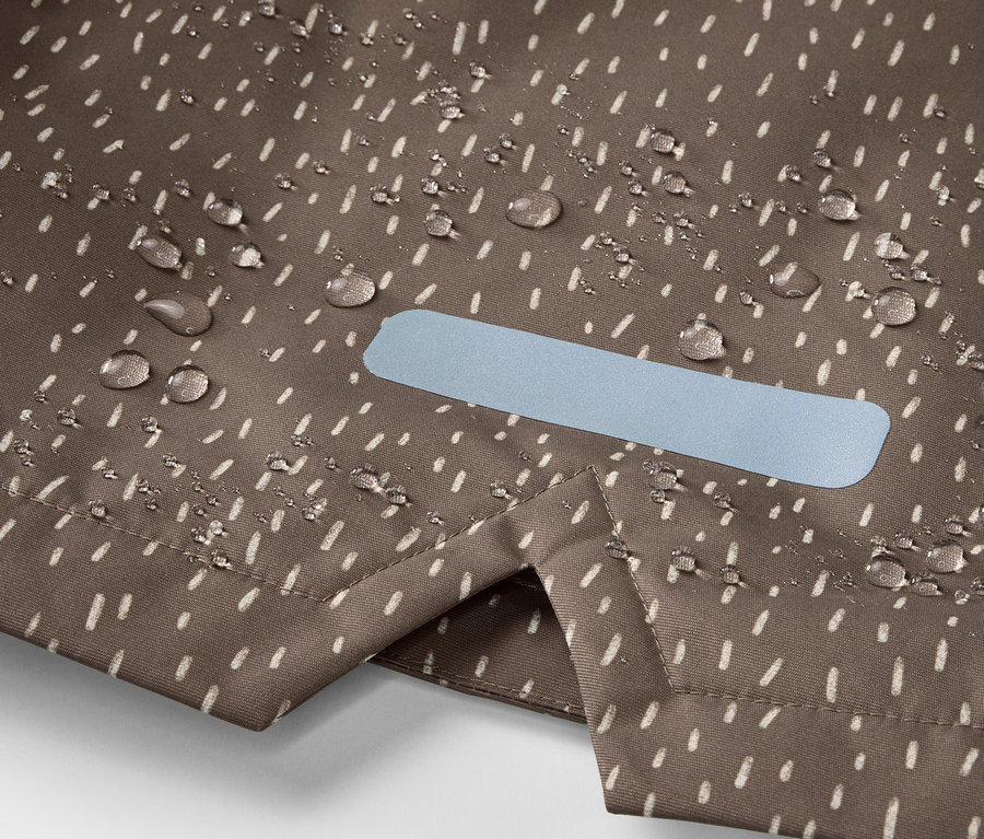 Gros plan sur une veste de pluie thermique pour enfant, avec des gouttes d'eau et un élément réfléchissant.