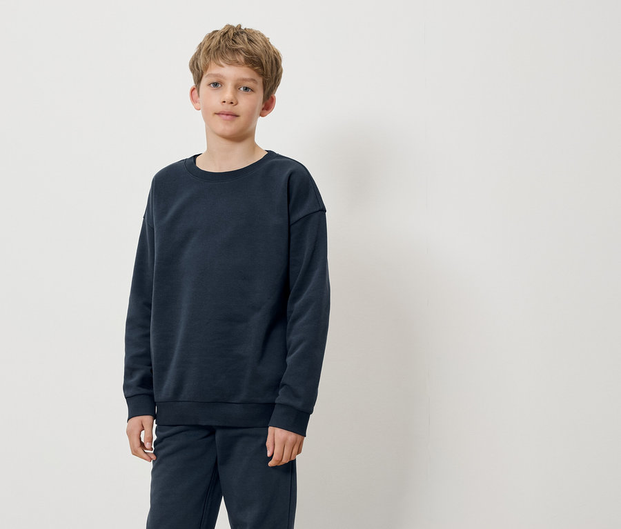 Un garçon debout portant un pull et un pantalon bleu marine.