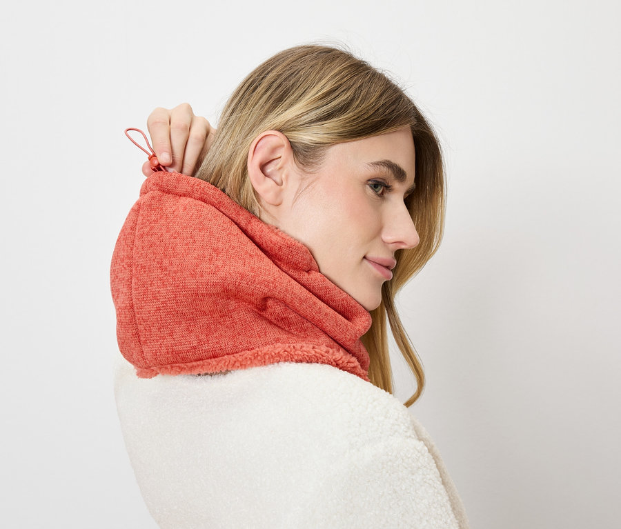 Femme ajustant capuche orange sur veste blanche.