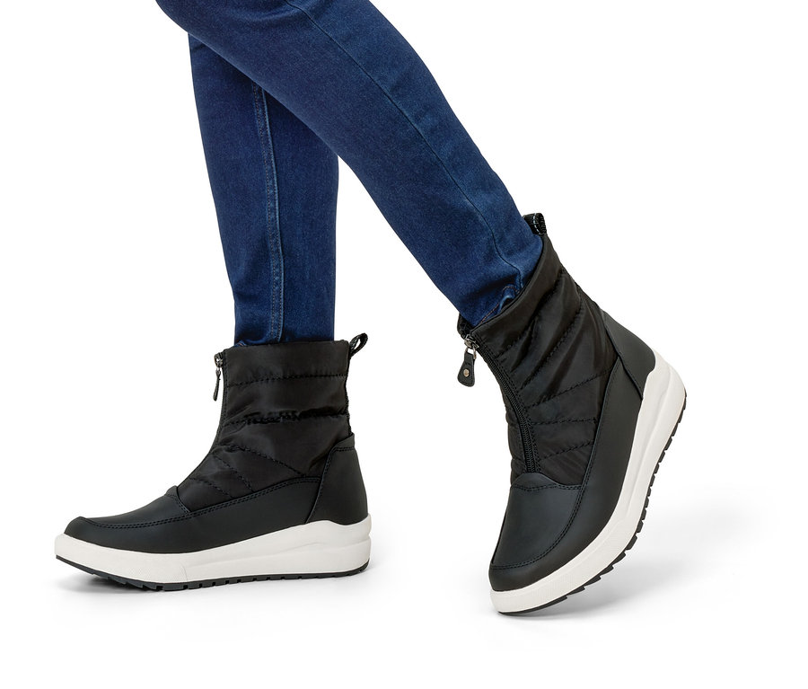 Jambes en jean et bottes d'hiver noires à semelles blanches.