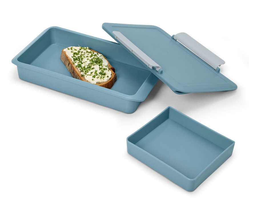 Une tartine aux herbes dans une boîte à déjeuner bleue avec couvercle et un récipient bleu vide.