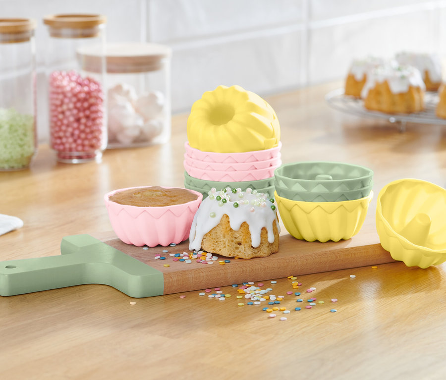 Moules à kouglof sur une planche à découper en bois avec des kouglofs finis et des décorations.