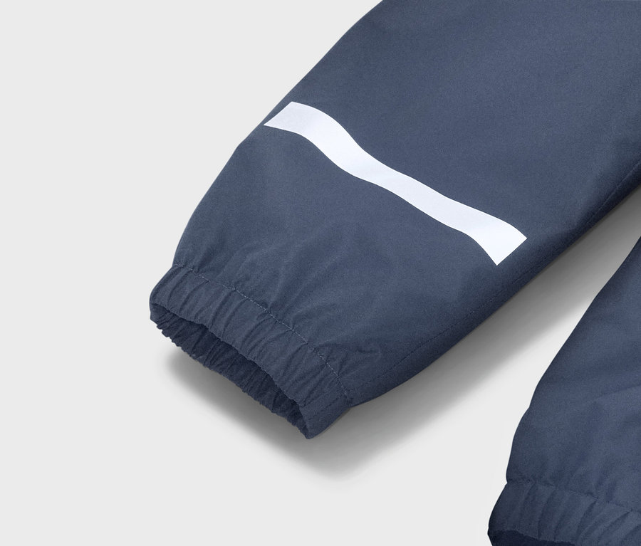 Vue détaillée de la manche bleue d'une veste avec une bande ondulée blanche et un poignet élastique.