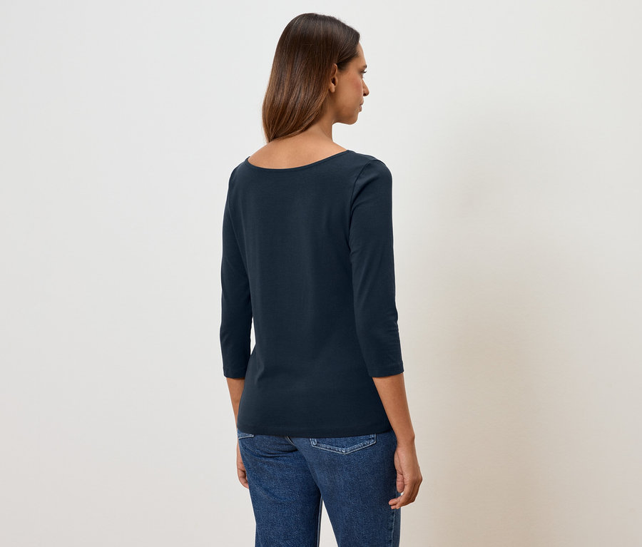 Une femme, dos à la caméra, porte un t-shirt bleu marine à manches trois-quarts et un jean.