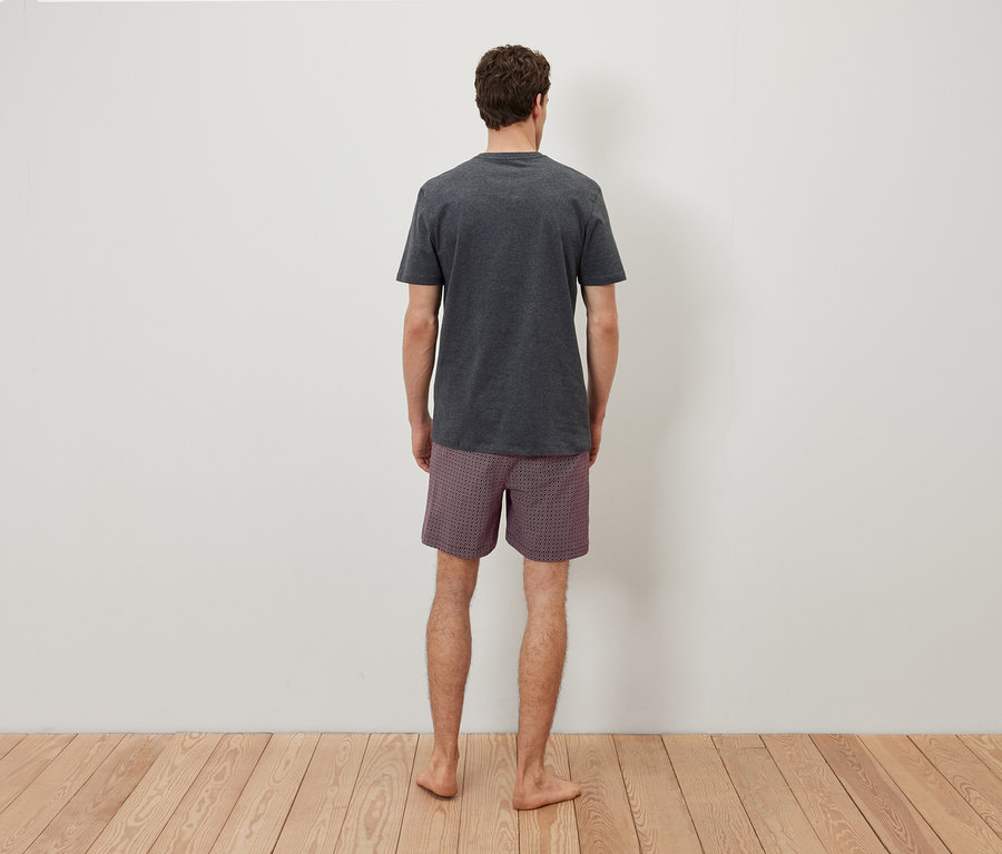 Un homme, vu de dos, porte un t-shirt gris et un short à carreaux.