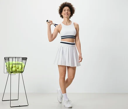 Femme tenant une raquette de tennis et portant une jupe de sport.