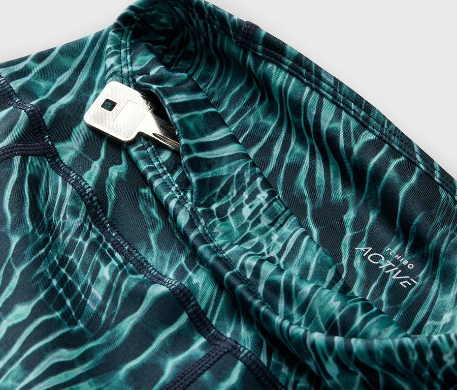 Gros plan sur un legging de sport vert à motifs avec une poche à clés dans laquelle se trouve une clé.